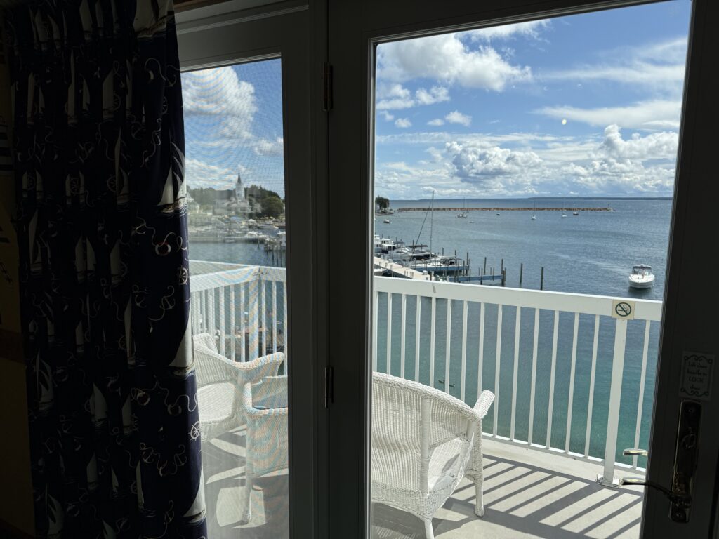 View from Chippewa Hotel Waterfront guest room looking out glass door to private balcony overlooking Mackinac Island harbor